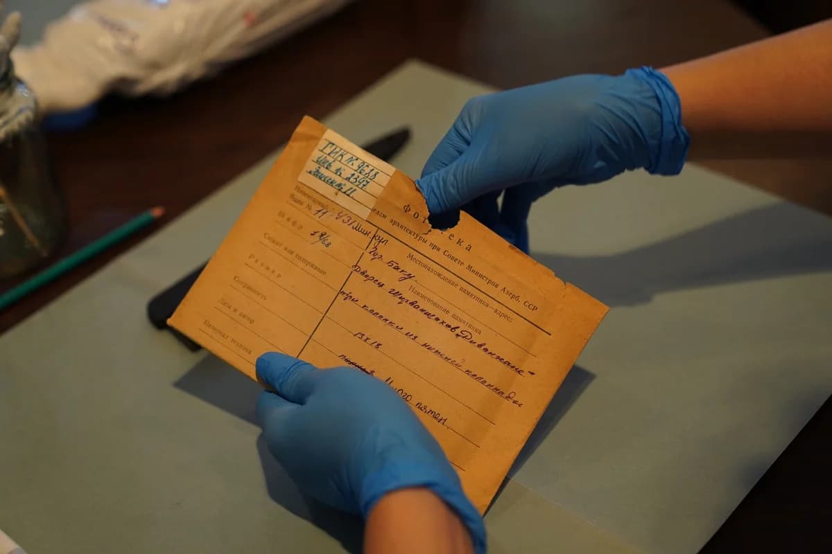 Blue-gloved hands handling an archival document on a desk.
