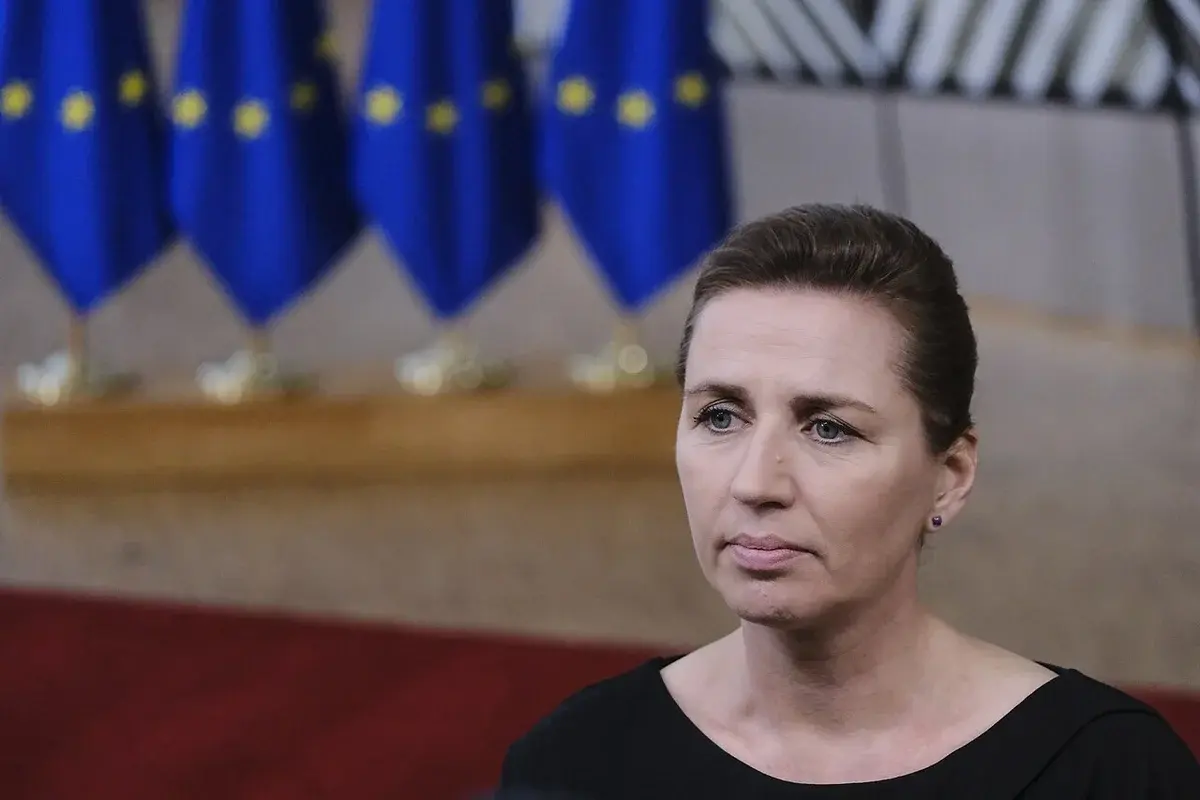 Portrait of Danish Prime Minister Mette Frederiksen in front of EU flags.