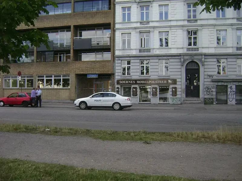 Danish police car parked on street next to red car with two men standing