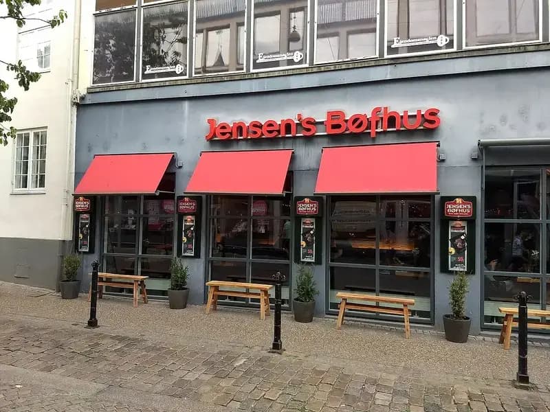 Exterior of Jensen's Bøfhus restaurant with red awnings and benches