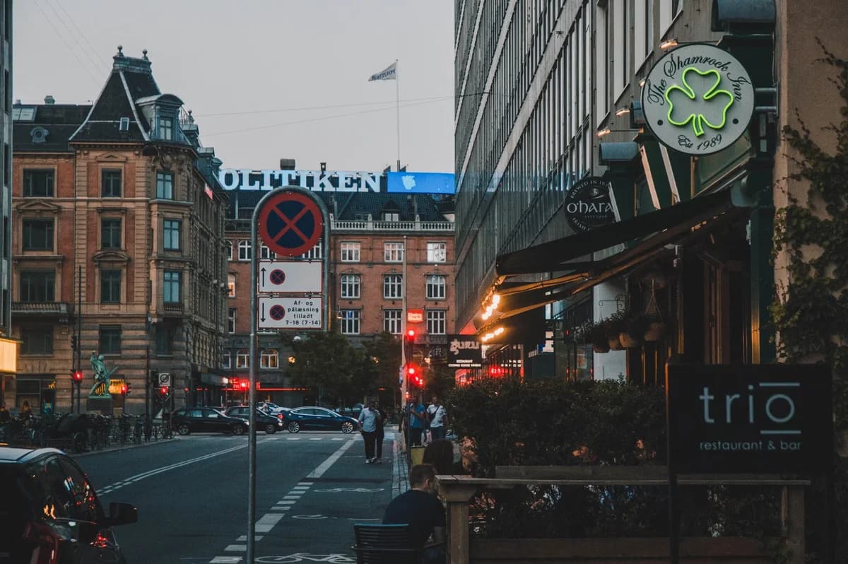 Evening street in Copenhagen with restaurants, cars, and pedestrians.