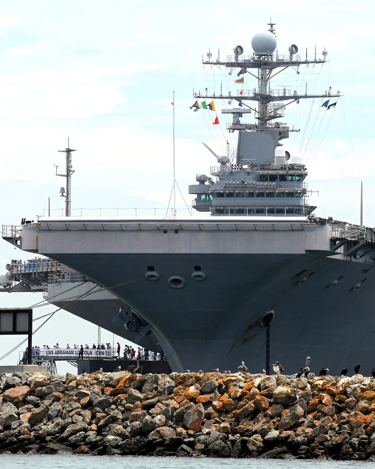 Aircraft carrier USS Abraham Lincoln docked at harbor with rocky shore in foreground