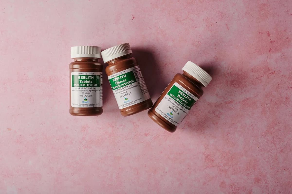 Three brown bottles of magnesium tablets on a pink background