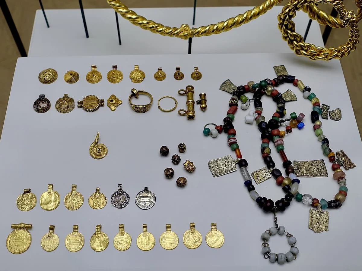 Viking Age gold and jewelry items including coins, arm rings, and beads displayed on a table