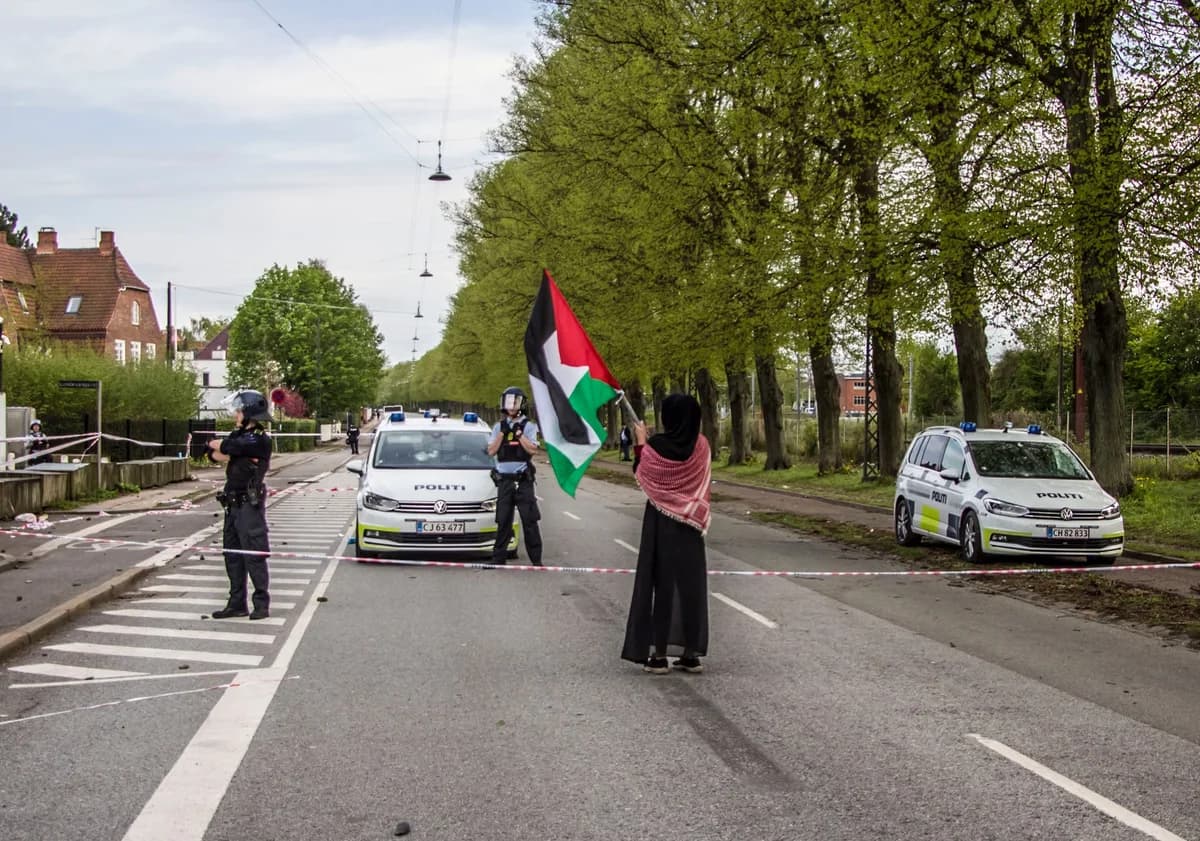 Woman holding Palestinian flag facing police on a tree-lined street
