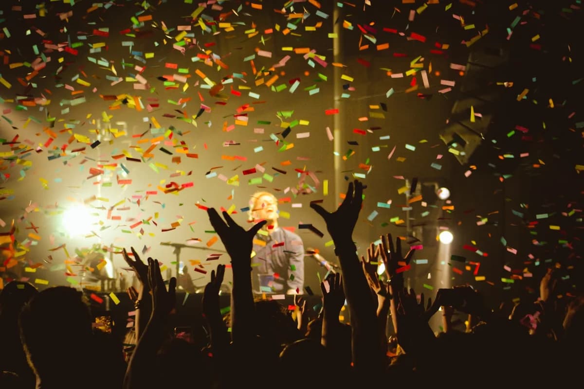 A concert crowd cheering under falling confetti.