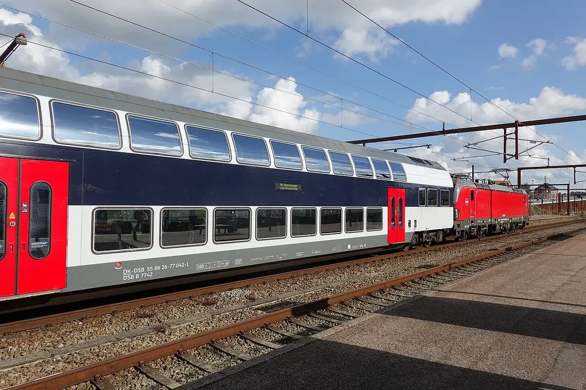 A red and white train at Næstved Station under a blue sky.