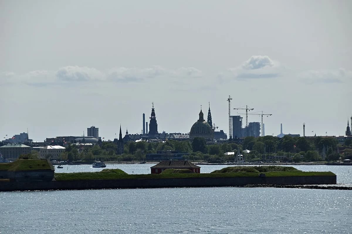 Copenhagen skyline seen across the waterfront with historic buildings and cranes in the distance.