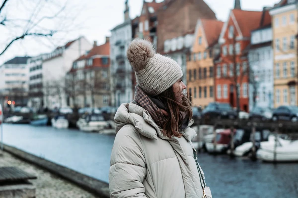 A woman in a knit hat and winter coat stands beside a canal in Copenhagen.