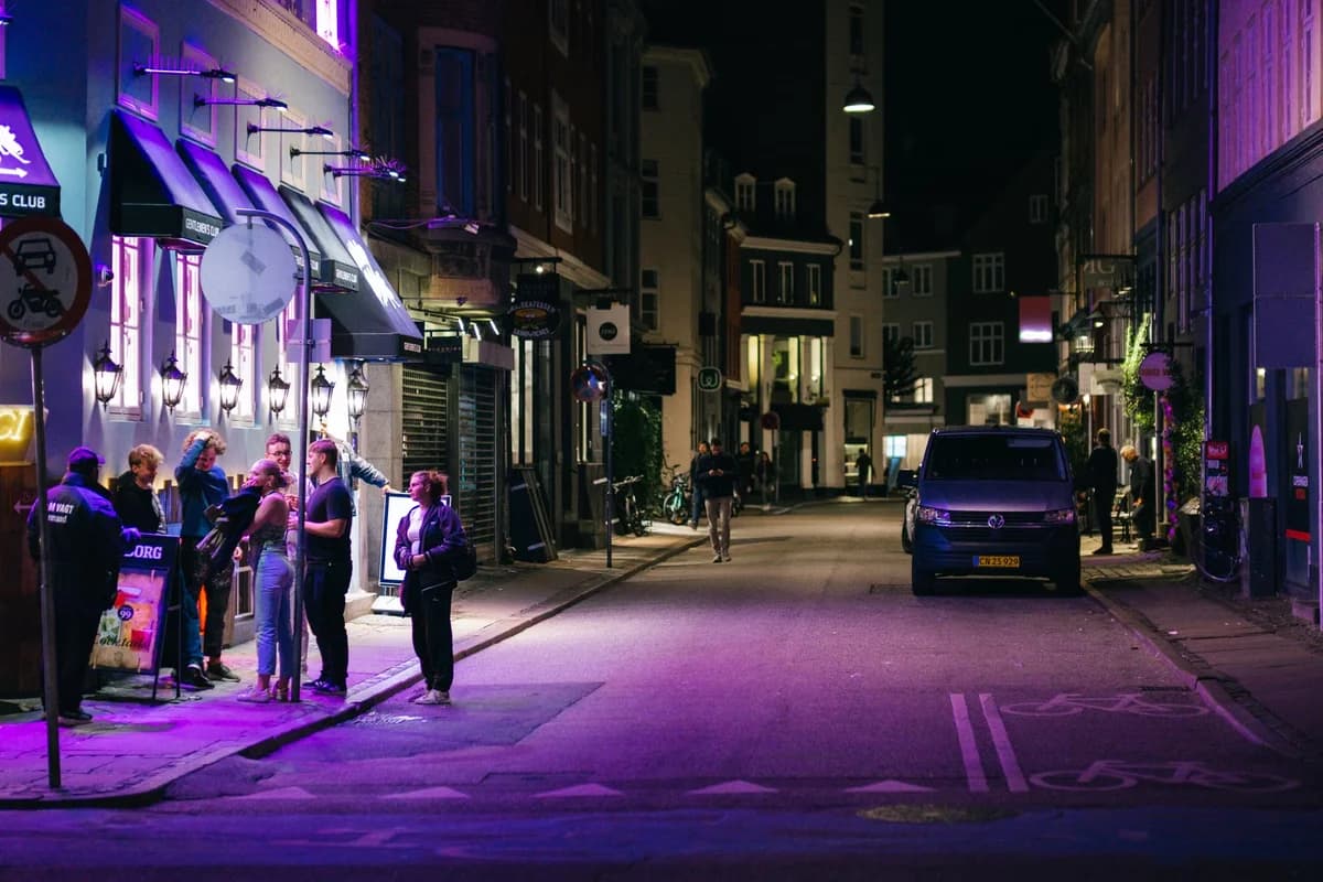 Group of people outside a building on a street lit with purple nighttime lights
