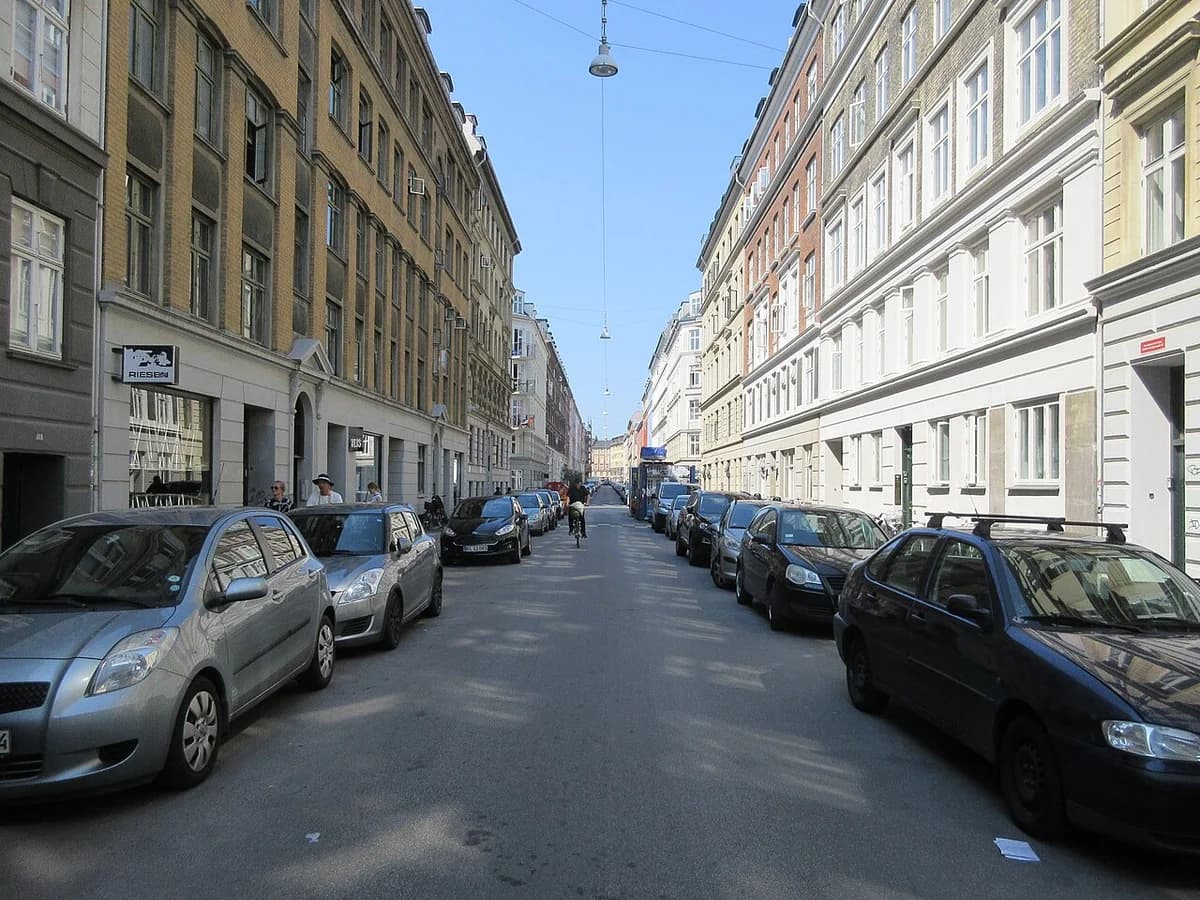 A narrow Copenhagen street lined with parked cars and apartment buildings.