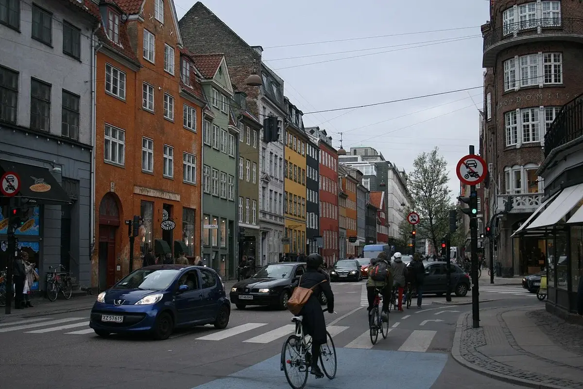 Street scene in central Copenhagen with colorful buildings, cars, and cyclists.