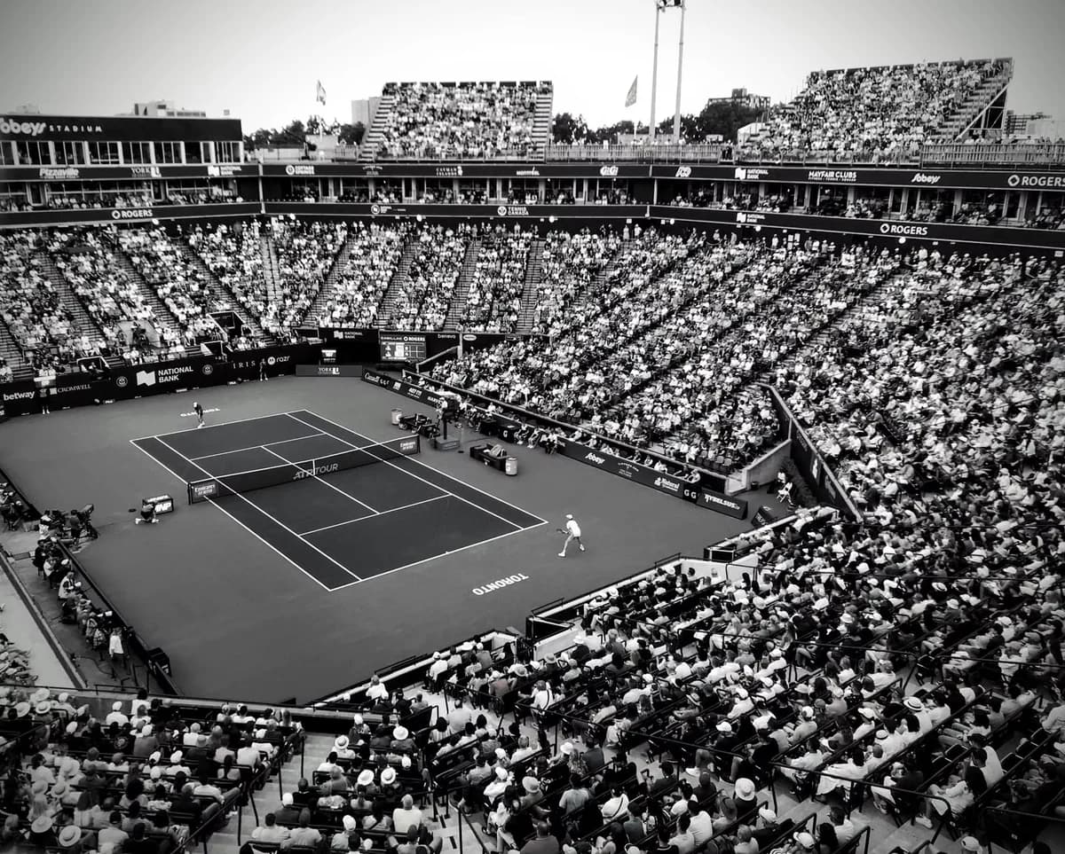 Black and white photo of a tennis match in a crowded outdoor stadium