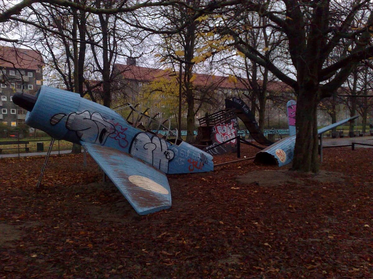 Graffiti-covered airplane-shaped playground equipment in a park.