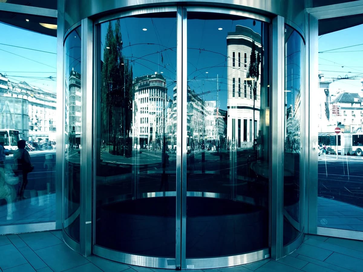 A glass revolving door reflecting a city street.